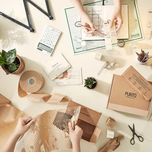 푸리토의 친환경 종이 포장 제작 및 디자인 과정을 보여주는 작업 장면 이미지 Purito’s eco-friendly packaging and design process shown from an overhead perspective