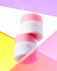 Two pink jars of hibiscus cream floating above vibrant colored acrylic panels