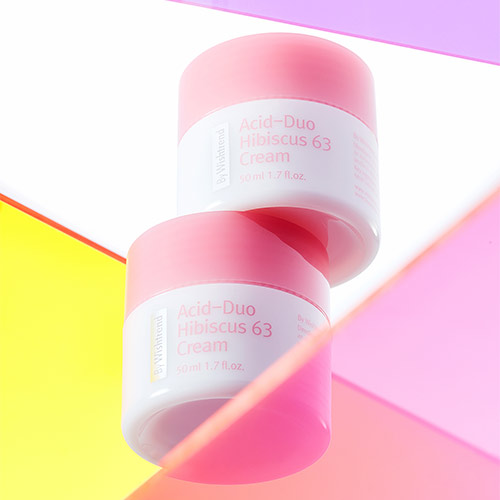 Two pink jars of hibiscus cream floating above vibrant colored acrylic panels