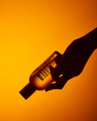 A hand holding ByWishtrend essence bottle against vivid orange background