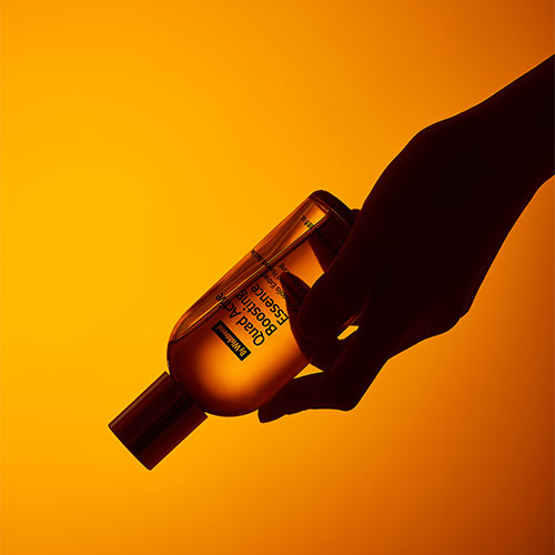 A hand holding ByWishtrend essence bottle against vivid orange background