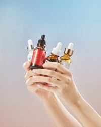 Hands holding multiple ByWishtrend ampoule bottles against soft gradient background