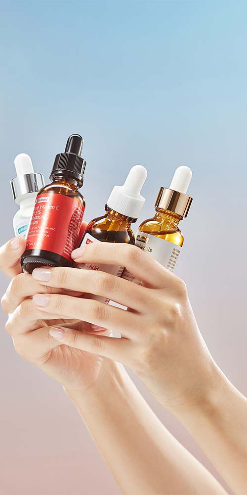 Hands holding multiple ByWishtrend ampoule bottles against soft gradient background