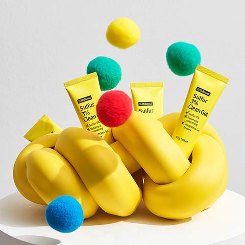 Sulfur spot treatment gel tubes with bouncing colorful balls on abstract yellow props