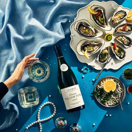 푸른 천 위에 진주, 굴, 샤블리 와인과 여성의 손이 함께 구성된 감각적 이미지 A refined image featuring Chablis wine, oysters, pearls, and a woman’s hand on a blue velvet backdrop