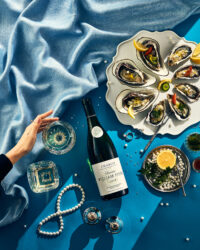 푸른 천 위에 진주, 굴, 샤블리 와인과 여성의 손이 함께 구성된 감각적 이미지 A refined image featuring Chablis wine, oysters, pearls, and a woman’s hand on a blue velvet backdrop