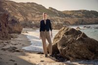 바닷가 절벽을 배경으로 선 채 바람을 맞고 있는 여성 모델의 전신 컷 A full-body portrait of a female model standing by a seaside cliff under sunlight