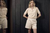 반팔 니트와 쇼츠를 착용한 모델이 블랙 벽 앞에 선 이미지 Model in beige knit top and shorts against dark wood wall
