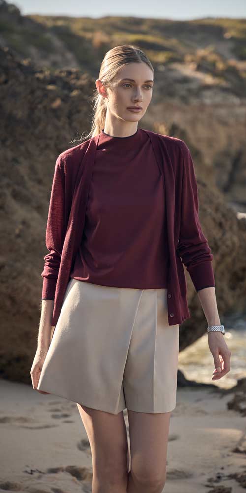 해변 배경에서 버건디 가디건과 베이지 쇼츠를 착용한 여성 모델 Model in burgundy cardigan and beige shorts on coastal backdrop
