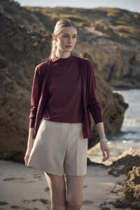 해변 배경에서 버건디 가디건과 베이지 쇼츠를 착용한 여성 모델 Model in burgundy cardigan and beige shorts on coastal backdrop