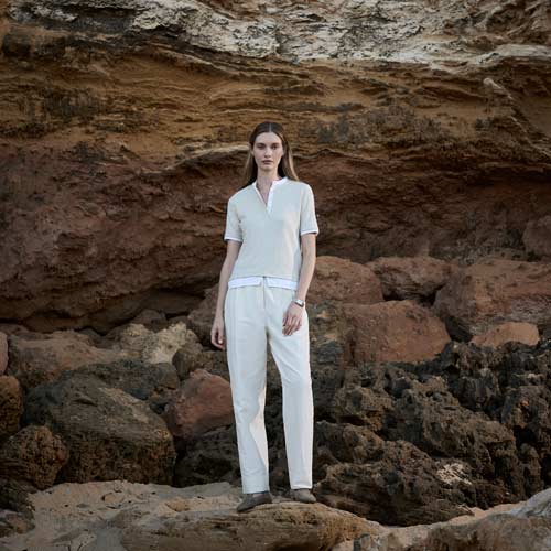 바위 절벽 앞에서 밝은 상의와 화이트 팬츠를 착용한 모델 Model in light shirt and white pants standing against a rugged cliff