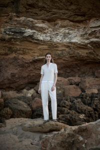 바위 절벽 앞에서 밝은 상의와 화이트 팬츠를 착용한 모델 Model in light shirt and white pants standing against a rugged cliff