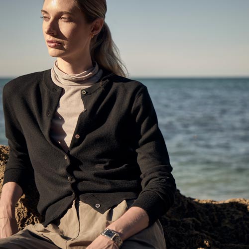 바닷가 바위 위에 앉아 카디건과 라이트한 이너를 입은 여성 모델 Woman seated on a coastal rock wearing a black cardigan over a light inner top
