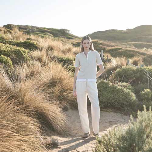 해안 언덕에서 린넨 팬츠와 밝은 니트를 착용한 여성 모델 Woman in light knit top and linen trousers standing among coastal bushes