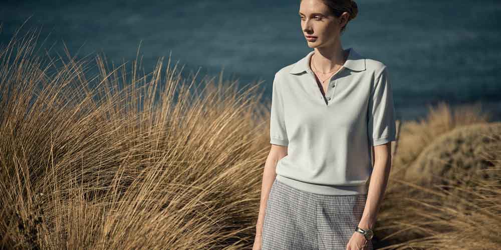 해안가 억새풀 배경에서 라이트 블루 니트 셔츠와 체크 쇼츠를 입은 모델 A model wears a sky-blue knit shirt and check shorts among Australian coastal grass