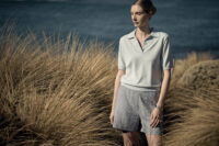 해안가 억새풀 배경에서 라이트 블루 니트 셔츠와 체크 쇼츠를 입은 모델 A model wears a sky-blue knit shirt and check shorts among Australian coastal grass