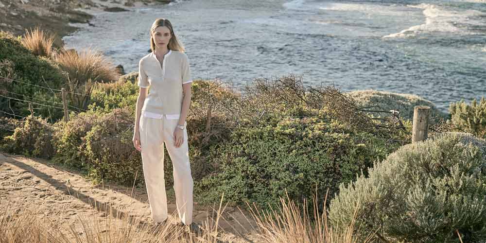 해안 절벽 위 베이지 니트 상의와 팬츠를 착용한 여성 모델 Female model in beige knit top and ivory trousers at a cliffside