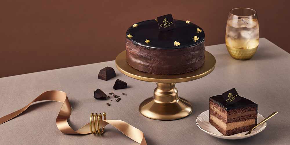 Godiva chocolate layer cake with a slice and golden ribbon on brown table