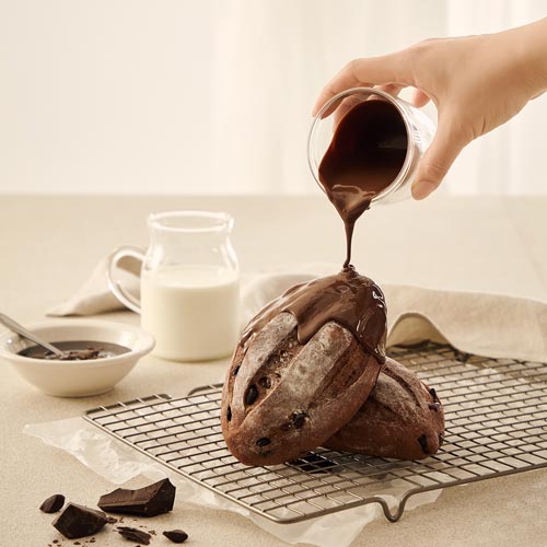 Hand pouring chocolate sauce over stacked chocolate breads