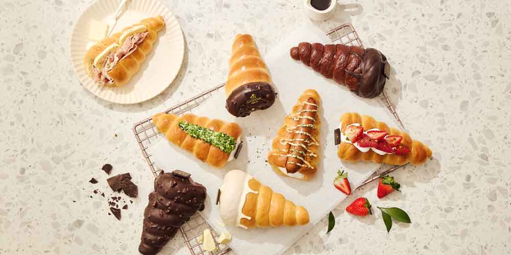 Flatlay of assorted Godiva cone breads with props like coffee, fruit, and crumbs