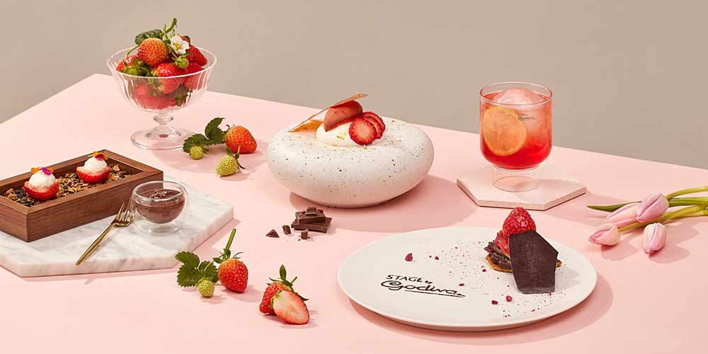 Godiva dessert display on pink background with strawberries and tulips