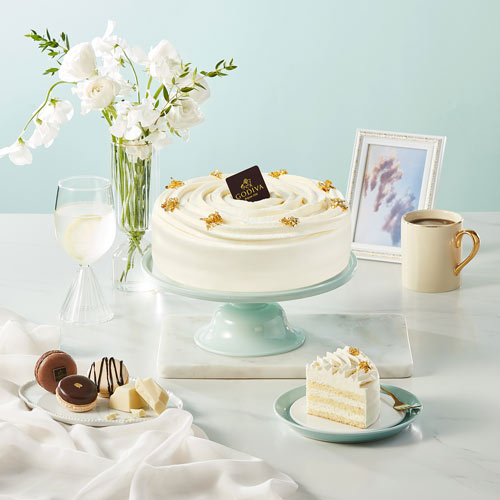 White cream cake with golden toppings on a pastel blue table Godiva cake photography by Studio AHNTONE