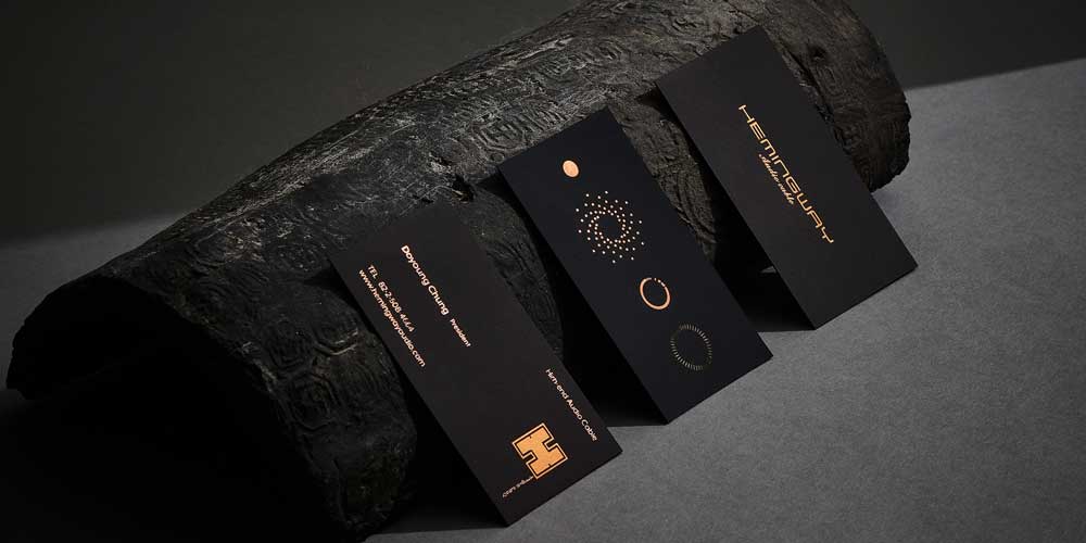 헤밍웨이 오디오 브랜드의 고급 명함 3종이 나무 위에 세워져 있음 Three luxurious business cards for Hemingway Audio displayed on a log