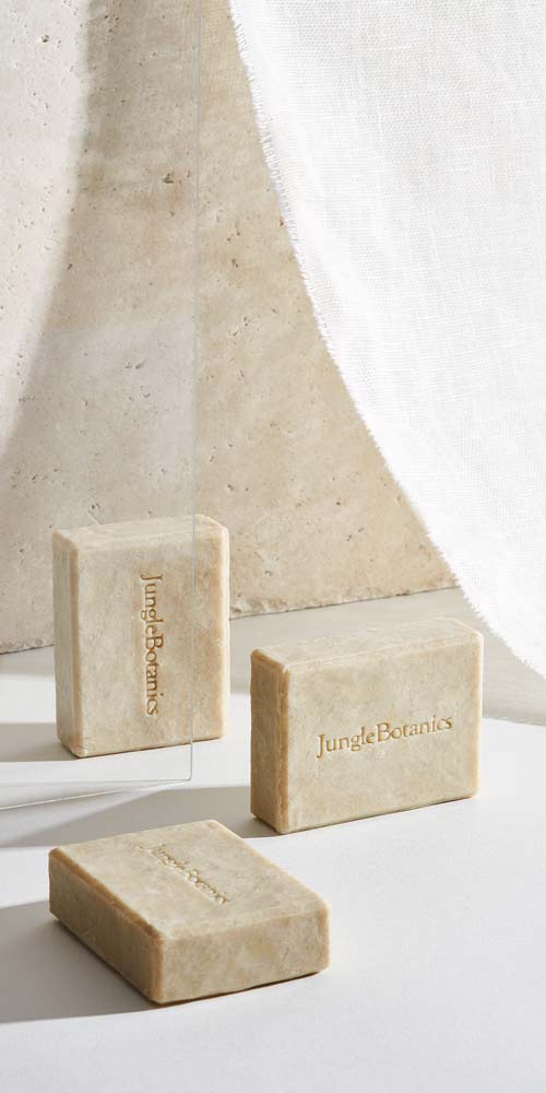 Jungle Botanics 비누가 유리에 반사되고 흰 천이 드리워진 연출 Jungle Botanics soaps reflected in a vertical glass pane with draped fabric
