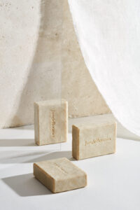 Jungle Botanics 비누가 유리에 반사되고 흰 천이 드리워진 연출 Jungle Botanics soaps reflected in a vertical glass pane with draped fabric