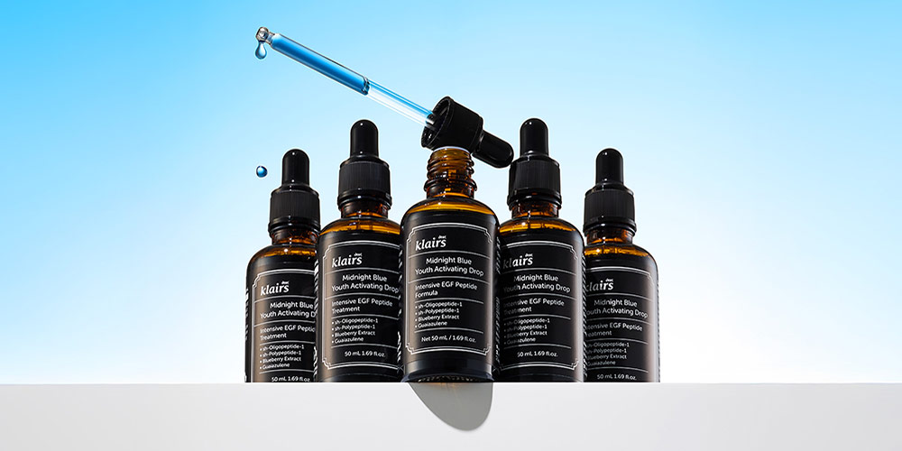 파란 드로퍼와 앰플 제품 5개가 배열된 Klairs 미드나잇 블루 시리즈 이미지 Still life of 5 Klairs blue serum bottles arranged with central dropper highlighting texture