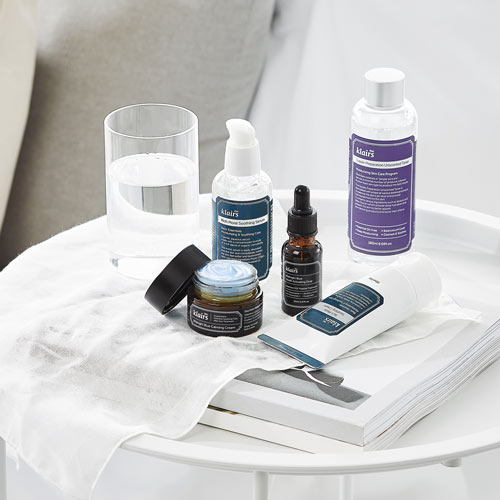 사이드테이블 위에 구성된 Klairs 스킨케어 제품들과 크림 텍스처 표현 이미지 Styled still life of Klairs skincare products on a bedside table