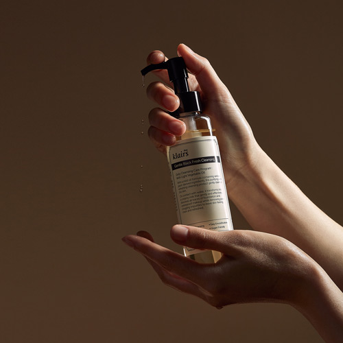 두 손으로 젠틀 블랙 클렌징 오일을 들어올린 장면 Hands holding a Gentle Black Cleansing Oil against a brown background