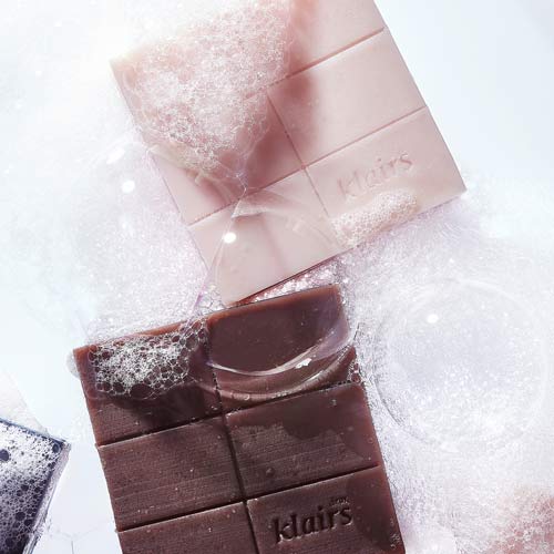 클레어스 비누 두 가지 색상이 거품 위에 놓인 모습 Two Klairs facial soaps placed on a bed of white bubbles