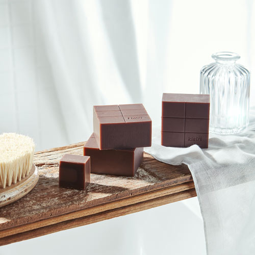 나무 질감 위에 정갈하게 배치된 Klairs 고체 비누 이미지 Still life of Klairs soap bars arranged on wood in natural daylight