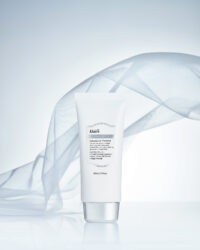 부드러운 천과 함께 연출된 클레어스 선크림 제품 이미지 Klairs sunscreen tube staged with flowing fabric and soft lighting