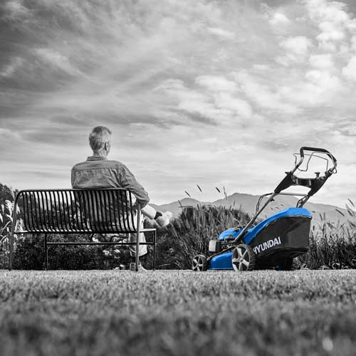 벤치에 앉아 잔디깎이를 바라보는 남성 모델의 흑백+컬러 연출 사진 Photo of a man sitting on a bench facing a lawn mower in black and white with color highlight