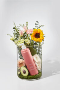 유리병 안에 꽃과 아보카도, 오제끄 바디로션이 함께 구성된 이미지 Floral arrangement in glass vase with avocado and Oseque body lotion bottle