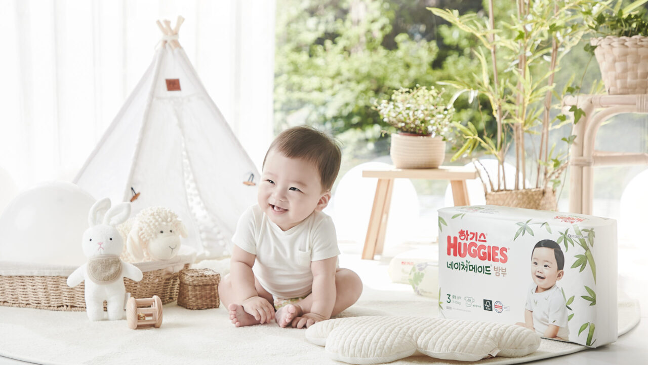 하기스 기저귀 패키지 옆에 앉아 웃고 있는 아기의 사진 Smiling baby sitting next to Huggies diaper pack in baby room