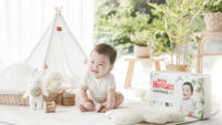 하기스 기저귀 패키지 옆에 앉아 웃고 있는 아기의 사진 Smiling baby sitting next to Huggies diaper pack in baby room