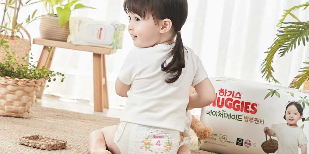 Girl in Diaper Looking Back Beside Huggies Diaper Pack