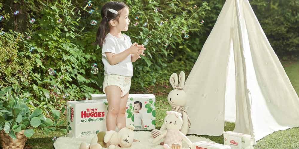 잔디밭에서 비눗방울을 바라보며 웃고 있는 여자아이와 하기스 네이처메이드 팬티형 기저귀 Girl wearing Huggies Nature Made panty-type diaper, smiling and looking at bubbles in an outdoor scene