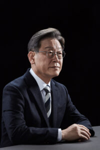 정면에 가까운 앵글로 테이블 앞에 앉아 단정한 자세를 취한 이재명 대통령 후보의 포트레이트 A composed and front-facing portrait of presidential candidate Lee Jae-myung seated at a table with a calm demeanor. Korean presidential election photo