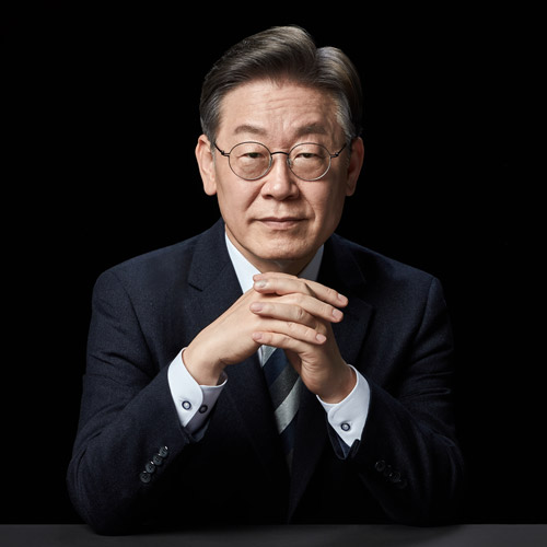 검은 배경 앞에서 두 손을 모으고 정면을 바라보는 이재명 대통령 후보의 포트레이트 A close-up portrait of presidential candidate Lee Jae-myung looking directly at the camera with hands clasped on a table against a black background