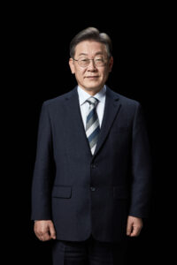 검은 배경 앞에 서서 정면을 바라보는 이재명 대통령 후보의 전신 포트레이트 A full-length front-facing portrait of presidential candidate Lee Jae-myung standing against a black background, Korean presidential election photo