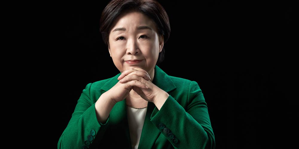 검은 배경 앞 책상에 앉은 심상정 대통령 후보의 공식 포트레이트 A formal portrait of presidential candidate Shim Sang-jung seated at a desk against a black background