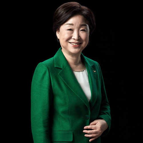 검은 배경 앞에서 반신으로 서 있는 심상정 대통령 후보의 미소 포트레이트 A half-body smiling portrait of presidential candidate Shim Sang-jung with a relaxed pose against a black background