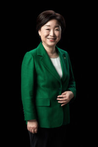 검은 배경 앞에서 반신으로 서 있는 심상정 대통령 후보의 미소 포트레이트 A half-body smiling portrait of presidential candidate Shim Sang-jung with a relaxed pose against a black background. Korean presidential election photo