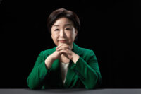 검은 배경 앞 책상에 앉은 심상정 대통령 후보의 공식 포트레이트 A formal portrait of presidential candidate Shim Sang-jung seated at a desk against a black background. Korean presidential election photo