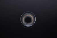 검은 배경 위에 놓인 렌즈미 블랙 컬러 콘택트렌즈의 클로즈업 이미지 Close-up photo of a black-colored LensMe contact lens placed on a black surface