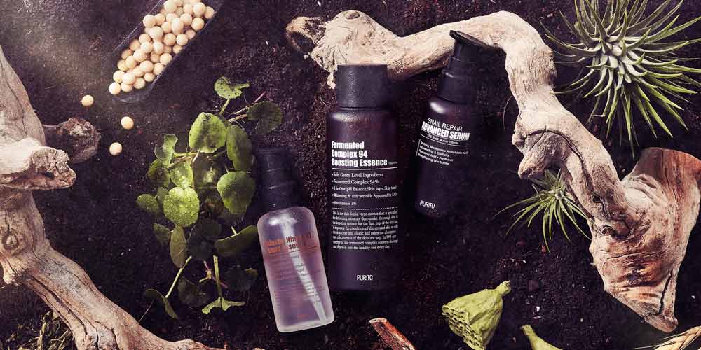 푸리토 스킨케어 제품 3종이 자연 흙과 나무, 생약 소재 위에 놓인 내추럴 플랫레이 Three Purito skincare products displayed on natural soil with botanical herbs and wood